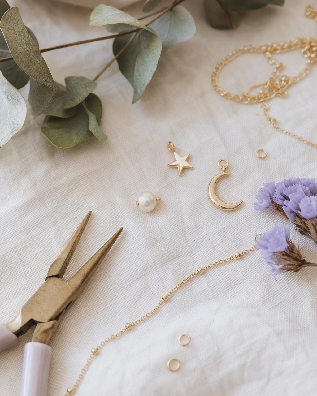 A flat-lay of gold chains, a pearl, star and moon charms with eucalyptus
